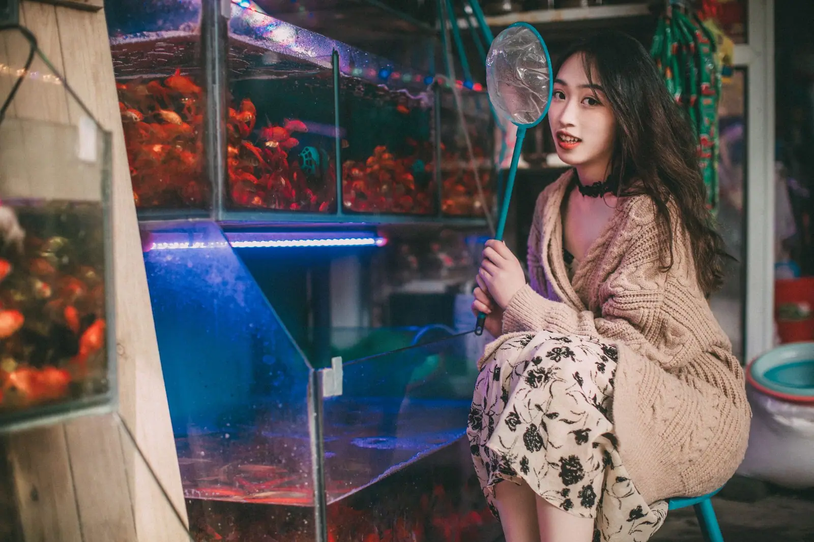 A woman holding a fish net beside rows of glass aquariums on display shelving