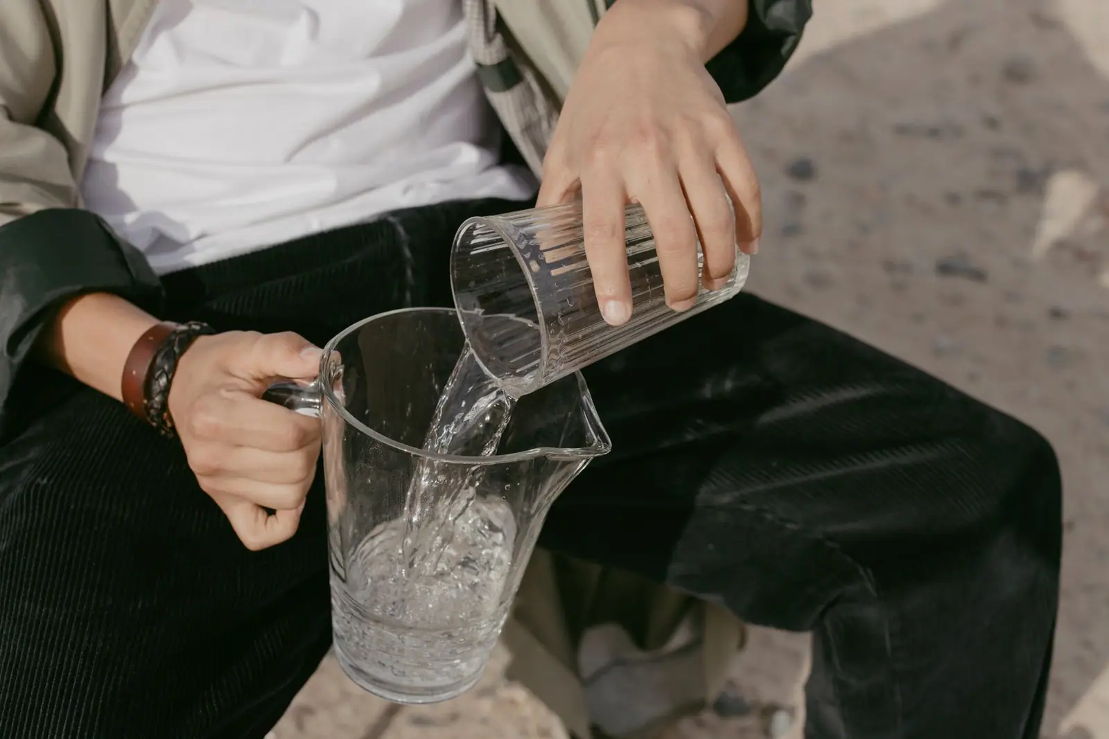 A person pouring water from a glass into a jug